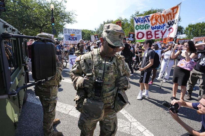 A first sergeant with the DC National Guard watches as activists protest Trump's federal takeover of policing of the capital, Saturday, Aug. 16, 2025, in Washington