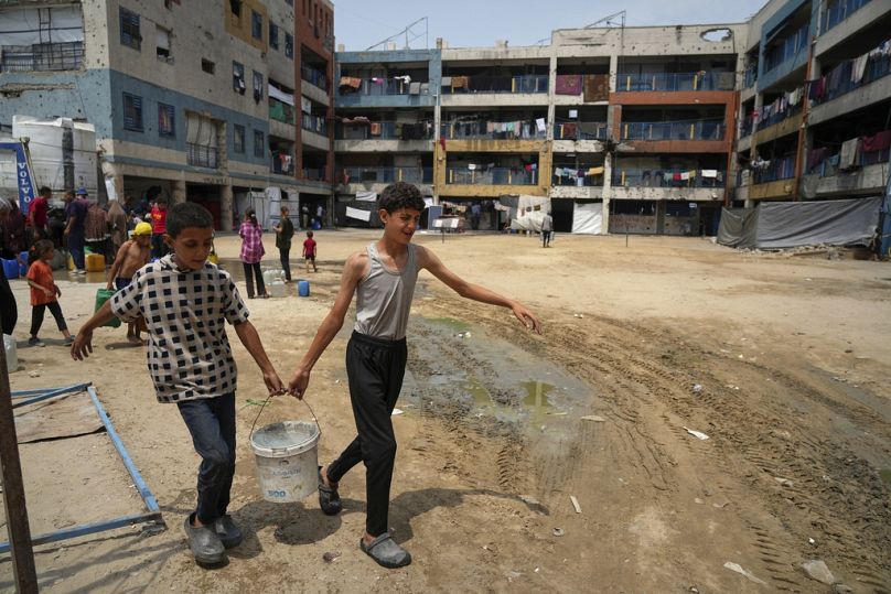 فتيان فلسطينيان يحملان دلو ماء جمعاه من نقطة توزيع في مدينة غزة، 12 أغسطس 2025.