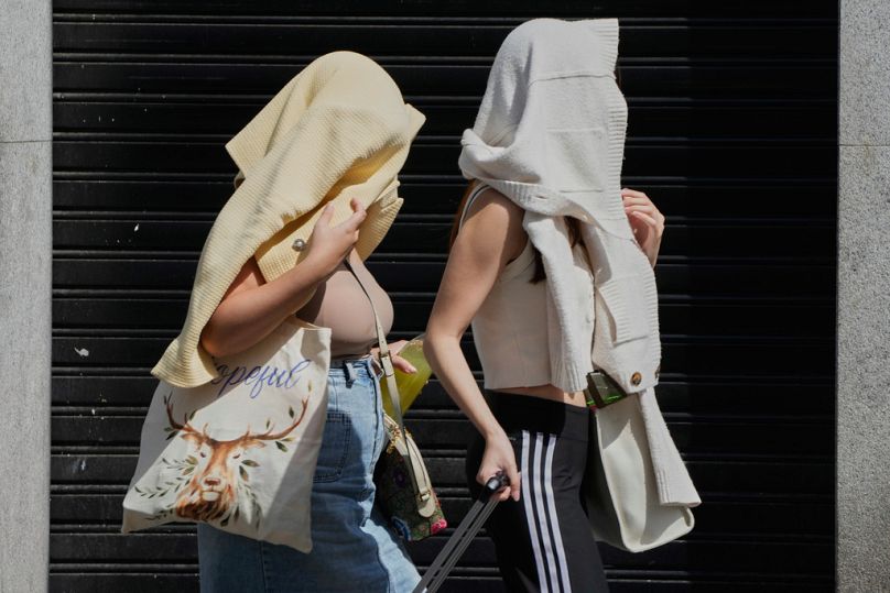 Duas mulheres caminham com a cabeça coberta para se protegerem do sol durante um dia extremamente quente em Madrid, Espanha, domingo, 17 de agosto de 2025.