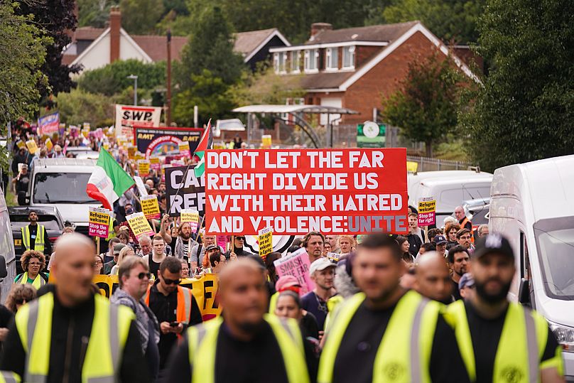 Demonstrators hold placards and banners as they leave a protest outside the Bell Hotel in Epping, 27 July, 2025