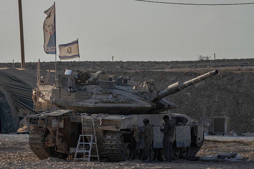 Israeli soldiers work on their tank parked in a staging area near the Israeli-Gaza border, as seen from southern Israel, Thursday, Aug. 21, 2025.