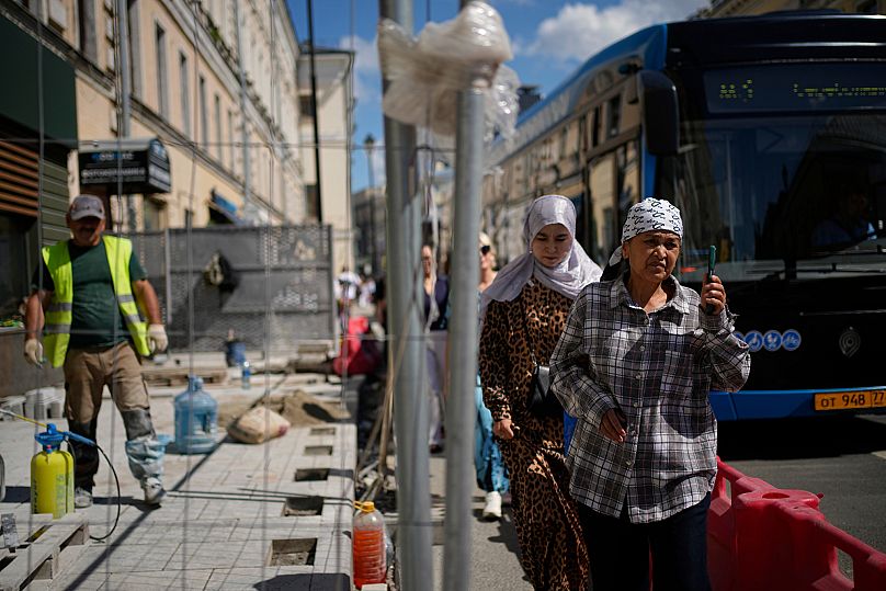 People walk along a street while a worker repairs pavement in Moscow, 6 August, 2025