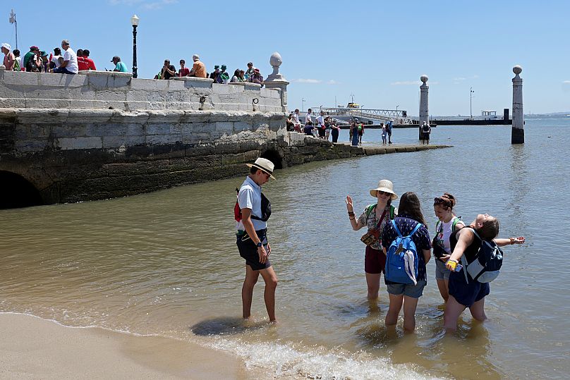World Youth Day pilgrims stand in the Tagus river water by Comercio square in Lisbon, 1 August, 2023