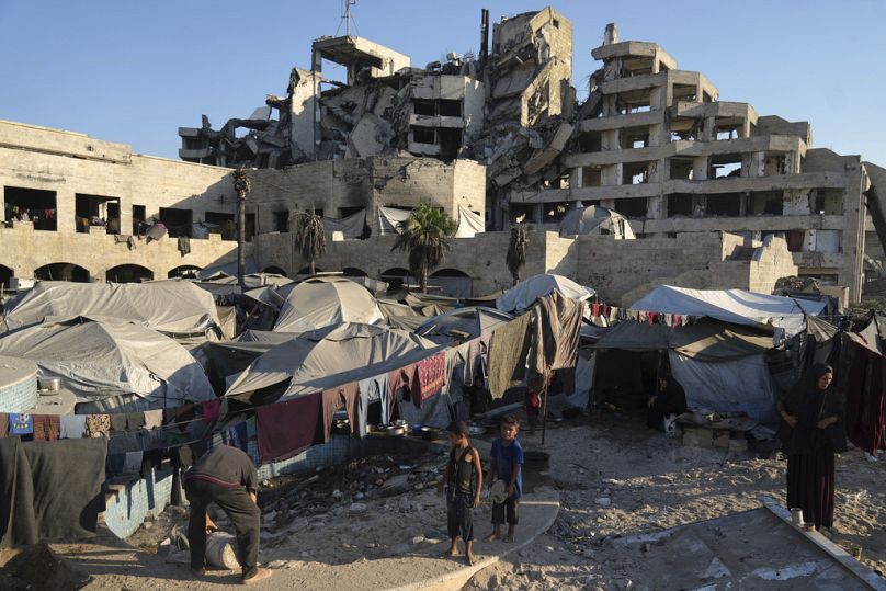 Palestinians stand by a makeshift tent camp located next to buildings destroyed during Israeli air and ground operations, in Gaza City, Saturday, Aug. 23, 2025
