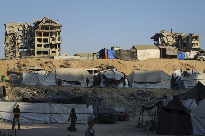 Palestinians walk on an area at a makeshift tent camp located next to buildings destroyed during Israeli air and ground operations, in Gaza City, Saturday, Aug. 23, 2025