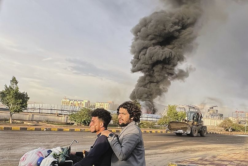 People ride a motorbike as smoke billows following Israeli air strikes on multiple areas including a power plant and a gas station in Sanaa, 24 August, 2025