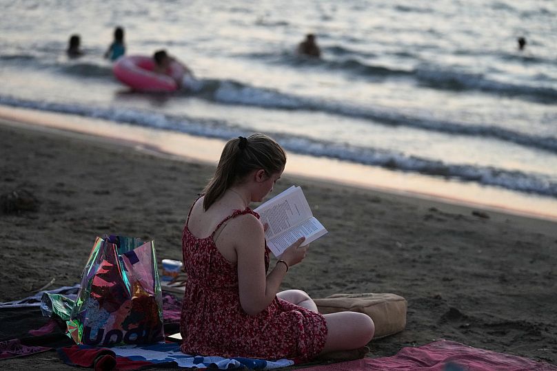 Μια γυναίκα διαβάζει ένα βιβλίο στην παραλία Καβούρι στη νότια Αθήνα, Ελλάδα, Δευτέρα, 11 Αυγούστου 2025. (AP Photo/Thanasis Stavrakis)