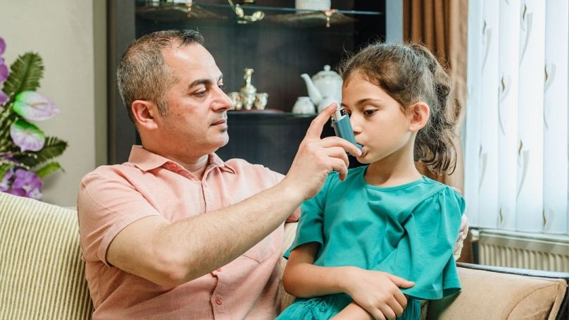 طفلة تتلقى مساعدة من والدها لاستخدام بخاخ الربو.