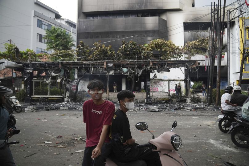 Uomini seduti su uno scooter vicino a un edificio incendiato durante le violente proteste contro il sussidio dei legislatori