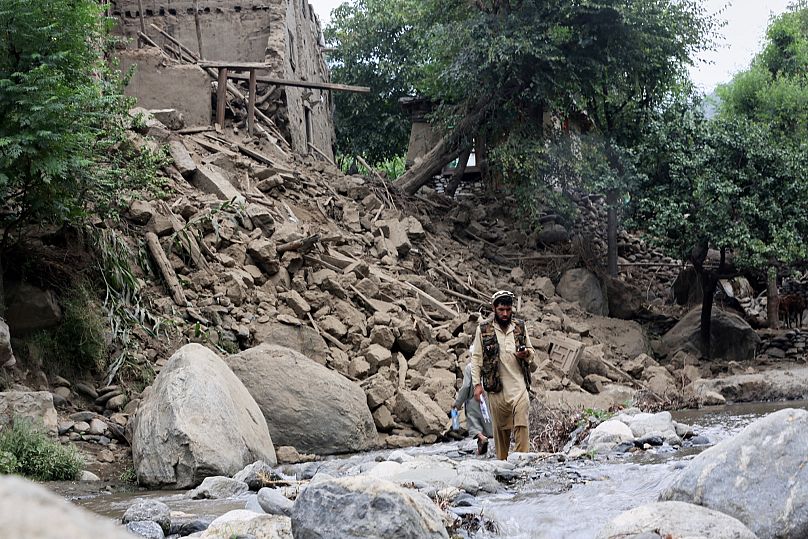 Bir adam ve bir çocuk, Afganistan'ın doğusunda, Kunar'ın Mazar Dara bölgesinde, depremde yıkılan bir evin yanındaki bir dereden geçiyor.
