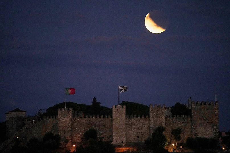 A lua cheia, ainda parcialmente obscurecida pela sombra da Terra após o eclipse lunar, nasce por detrás do Castelo de São Jorge, em Lisboa.