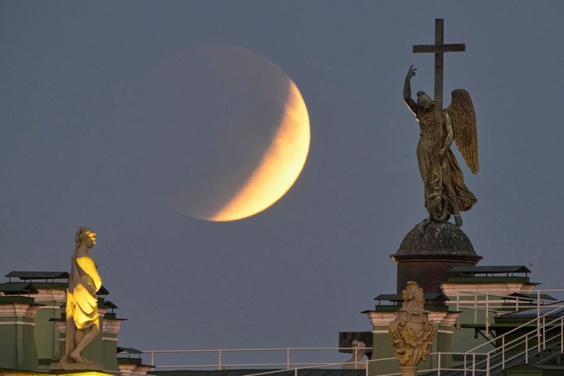 La luna llena sale detrás de una estatua de un ángel situada en lo alto de la Columna de Alejandro, en la Plaza del Palacio, durante un eclipse lunar total en San Petersburgo.