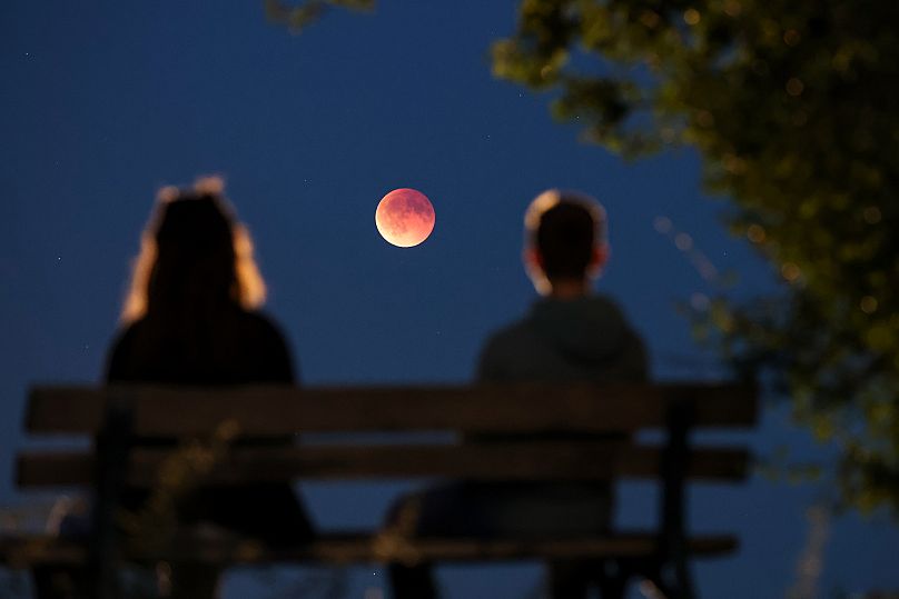 Onlookers watch the total lunar eclipse, also known as the blood moon, from a park bench, in Leipzig, Germany, Sunday, Sept. 7, 2025. 