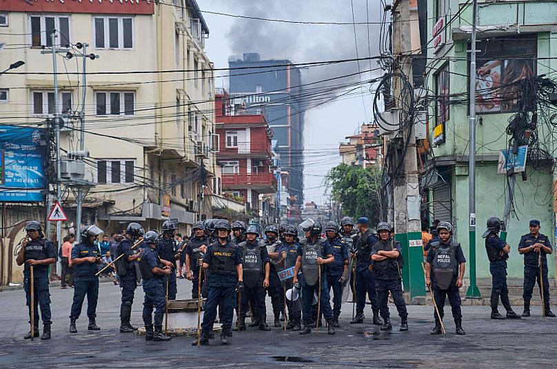 Nepalese police stand guard as smoke rises from the burnt Hilton hotel in Kathmandu, 10 September, 2025