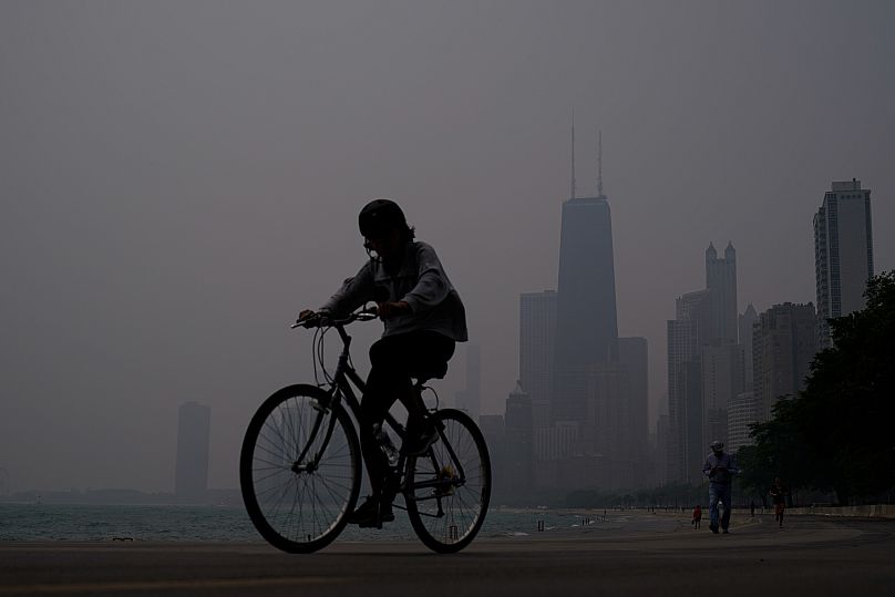 A person rides a bicycle along the shore of Lake Michigan as the downtown skyline is blanketed in haze from Canadian wildfires June 27, 2023.