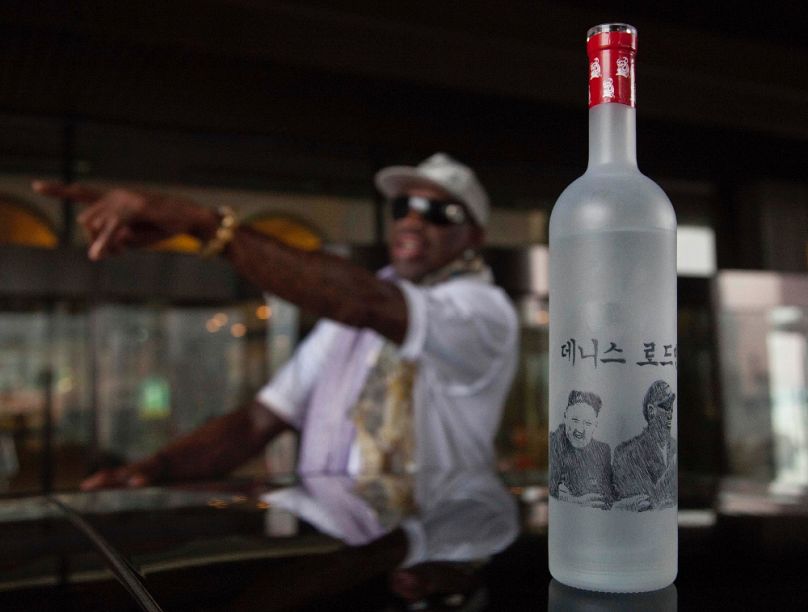Egy kézzel illusztrált vodkásüveg Kim Dzsongun és Dennis Rodman arcmásával egy phenjani szálloda előtt – a háttérben a kosarazó, 2014. január 7-én