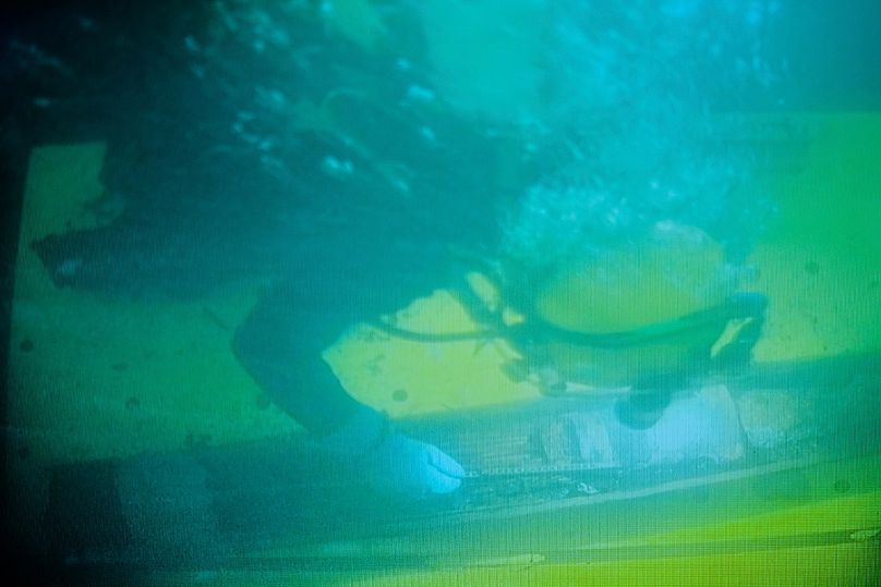 In this photo taken from a surveillance monitor, a diver works on a 128-millimeter artillery grenade