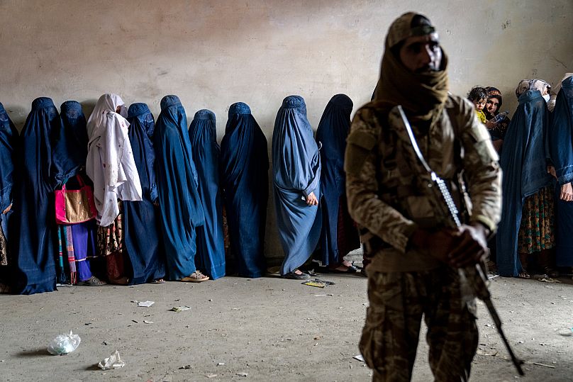 A Taliban fighter stands guard as women wait to receive food rations distributed by a humanitarian aid group in Kabul, 23 May, 2023
