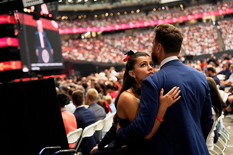 Os participantes ouvem o presidente Donald Trump, no ecrã à esquerda, discursar numa cerimónia em memória do ativista conservador Charlie Kirk no State Farm Stadium