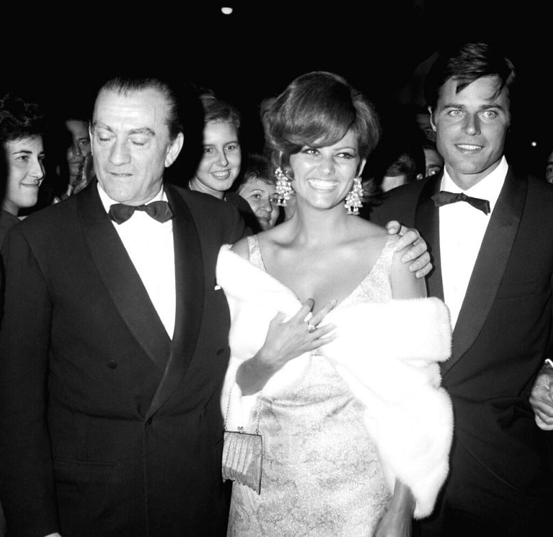 Da sinistra a destra in prima fila: il regista italiano Luchino Visconti, l'attrice italiana Claudia Cardinale e l'attore francese Jean Sorel arrivano al Movie Palace sul Lido