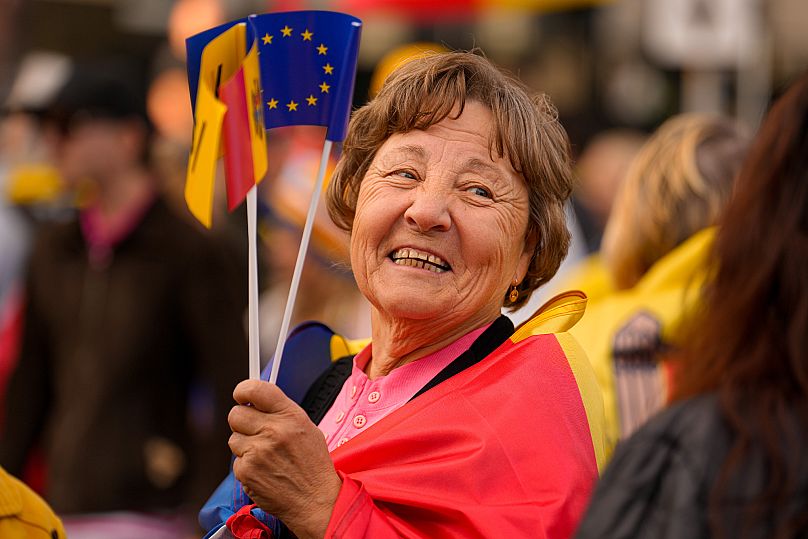 A woman smiles as she holds Moldovan and EU flags during a pro-EU rally of the ruling Party of Action and Solidarity in Chișinău, 26 September, 2025