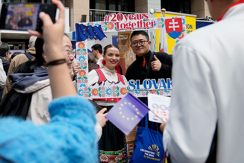 A family takes a photo of a relative standing in a frame of Slovakia with a traditionally dressed woman in Brussels, 4 May, 2024
