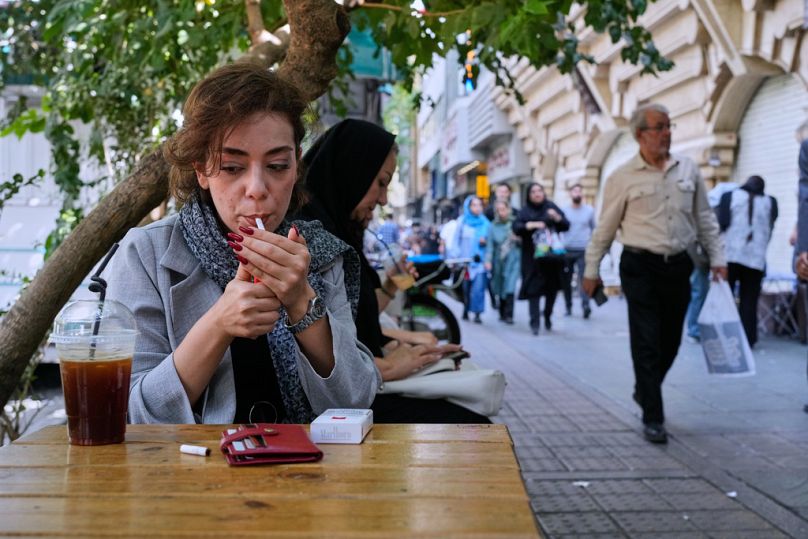 A woman lights a cigarette in the alfresco dining area of a cafe at the Enqelab-e-Eslami (Islamic Revolution) street, in Tehran, Iran, Saturday, Sept. 27, 2025