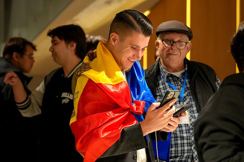 A supporter of the pro-EU Party of Action and Solidarity (PAS) draped in the Moldovan flag smiles as he checks partial results on a phone after the polls closed.