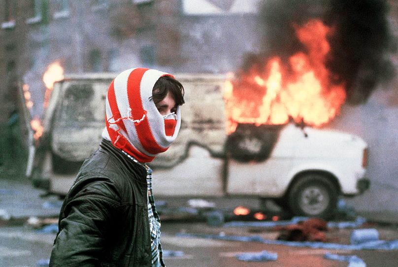 A youth wearing a hooded mask stands near a burning truck during the violence after the death of hunger strikers at Maze Prison in Belfast, 1981 