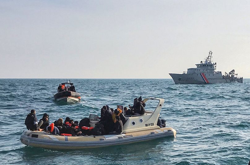 Menekültek csónakja a Brit Csatornában, a háttérben járőrhajóval