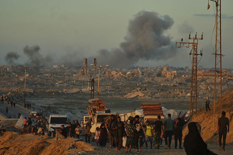 Smoke rises following an Israeli military strike in the background as displaced Palestinians flee northern Gaza, 1 October, 2025