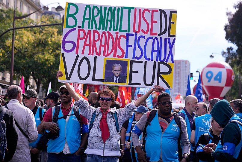 A demonstrator holds a poster of LVMH CEO Bernard Arnault reading "B Arnault uses 6 tax havens, thief" in Paris, 2 October, 2025 