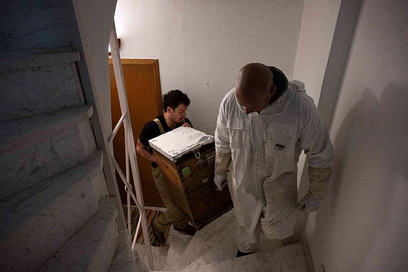 Grigoris Melas, foreground, and Konstantinos Pantoudis carry a beehive during a late-night transfer to a building's rooftop, in the Vyronas suburb of Athens, Greece.