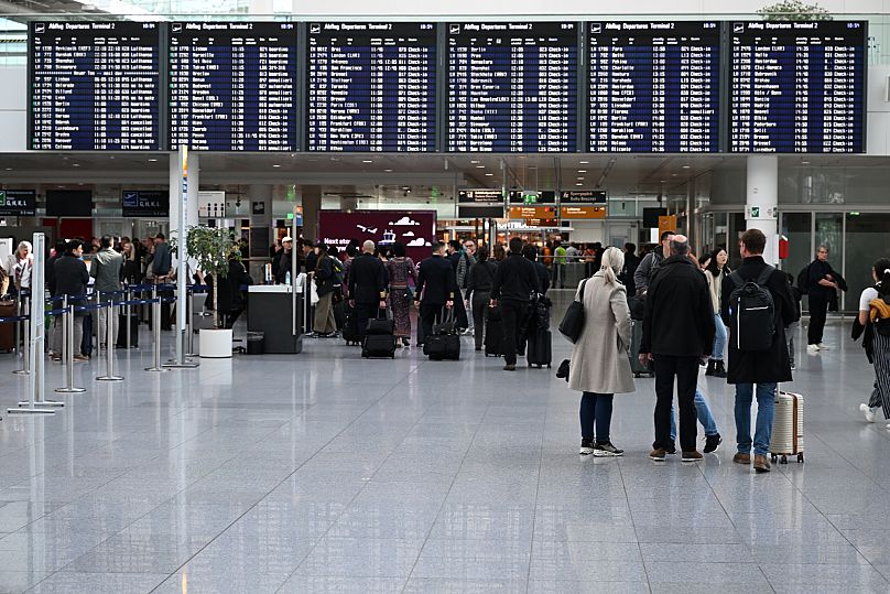 Passengers stand in front of a display board in Terminal 2 at Munich Airport, 3 October, 2025