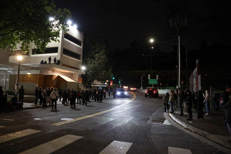 Federal agents stand on the roof as people protest outside a U.S. Immigration and Customs Enforcement facility in Portland, Oregon, Friday, Oct. 3, 2025. (AP Photo/Amanda Loma