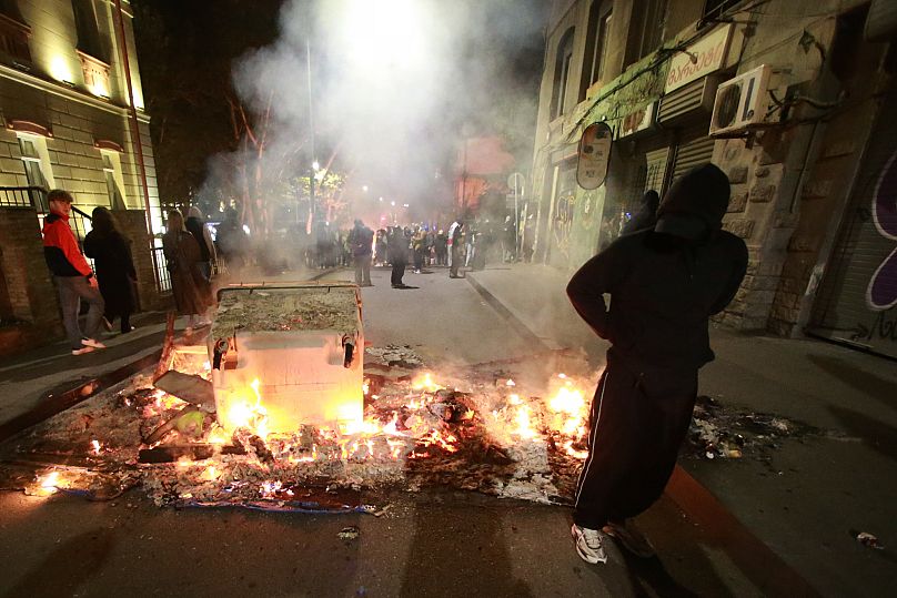 A demonstrator stands behind a burning barricade not far from a police line during an opposition rally in the city center of Tbilisi, Georgia, on Sunday, Oct. 5, 2025
