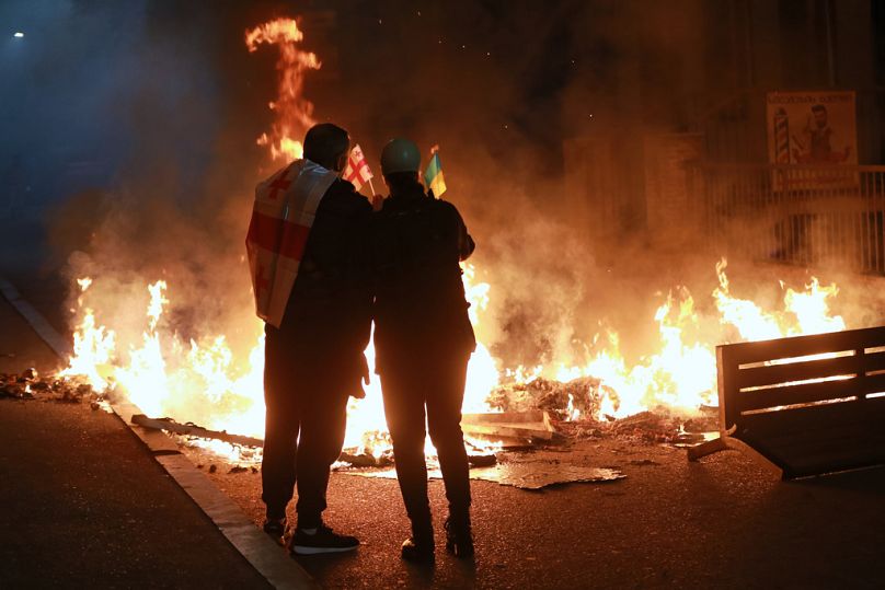 Protesters with Georgian and Ukrainian flags stand behind a burning barricade during an opposition rally in the city center of Tbilisi, Georgia, on Saturday, Oct. 4, 2025