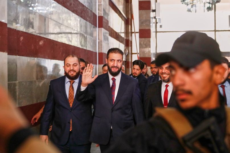 Syrian interim President Ahmad al-Sharaa waves as he enters a polling station where electoral members are voting in a parliamentary election in Damascus, Sunday, Oct. 5, 2025