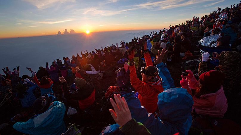 In this Sunday, Aug. 11, 2013 photo, thousands of hikers cheer from the summit of Mount Fuji in Japan as the sun rises. 