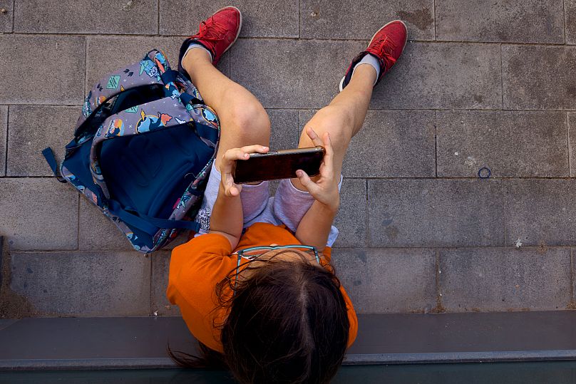 Un garçon de 11 ans joue avec le téléphone de son père devant son école à Barcelone, en Espagne, le lundi 17 juin 2024. 