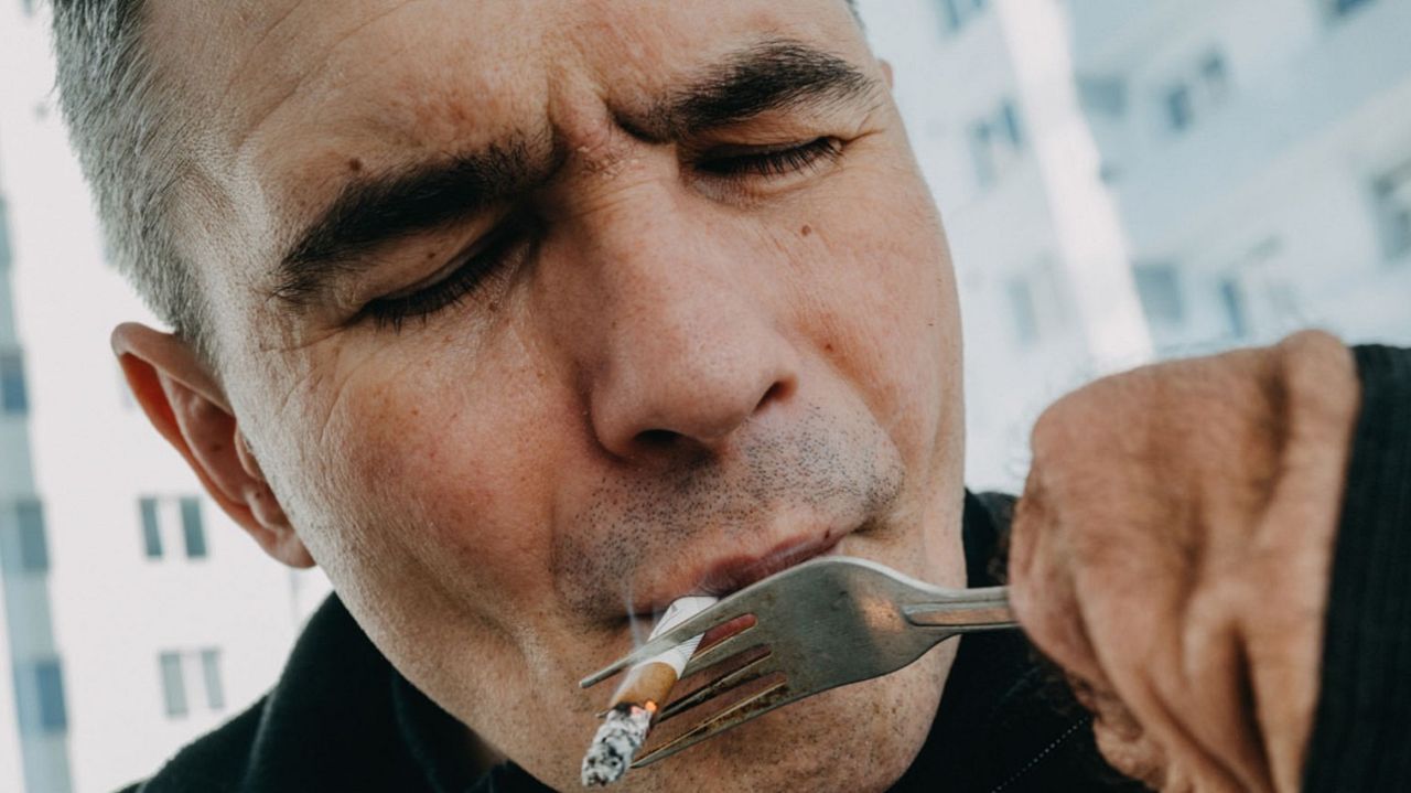 Vyacheslav Levitsky smokes a cigarette, holding it with a fork attached with a rubber band to the stump of his forearm. He lost his limbs due to injuries and frostbite in Russian captivity.