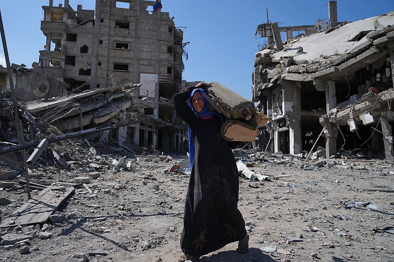 An elderly displaced Palestinian woman carries an item past destroyed buildings in Khan Younis, 10 October, 2025