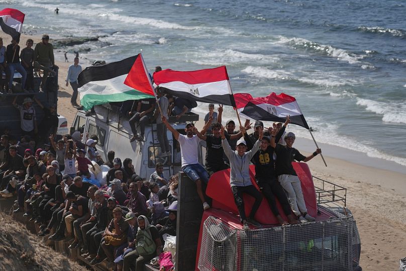 Des Palestiniens déplacés montent sur des camions et brandissent des drapeaux égyptiens et palestiniens le long de la route côtière près de Wadi Gaza, samedi 11 octobre 2025.