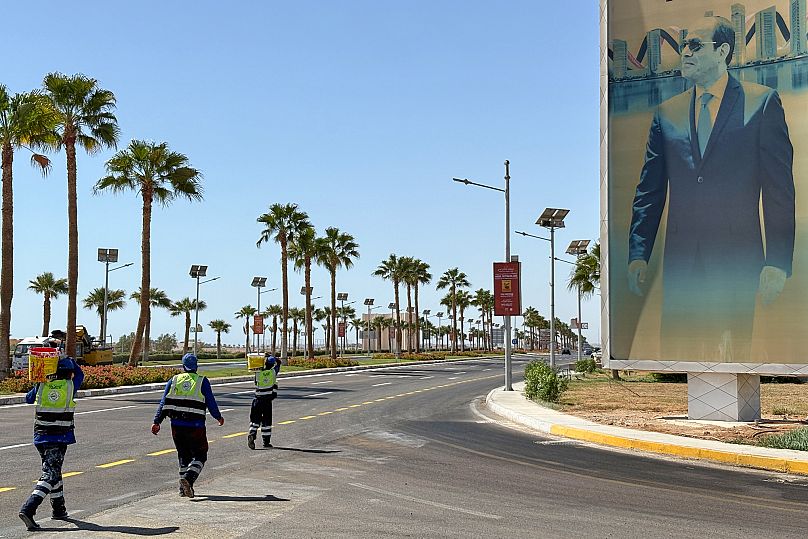 Workers carry paint as they walk past a banner showing Egyptian President Abdel-Fattah el-Sissi at the Red Sea city of Sharm el-Sheikh, Egypt, Saturday, Oct. 11, 2025