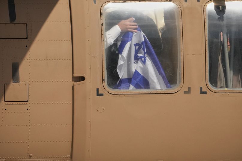 أحد الرهائن الإسرائيليين الذين أُفرج عنهم يرفع علم إسرائيل من داخل مروحية عسكرية بعد إطلاق سراحه من أسر حركة حماس في قطاع غزة، يوم الاثنين 13 أكتوبر 2025.