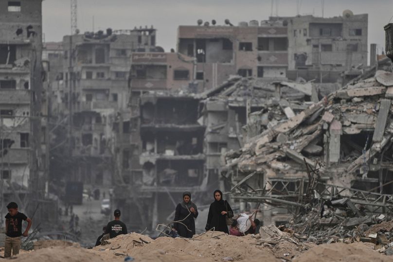 فلسطينيون يسيرون قرب مبانٍ مدمّرة في مخيم الشاطئ بمدينة غزة، بعد اتفاق حماس وإسرائيل على هدنة تشمل إطلاق سراح الرهائن المتبقّين، الأحد 12 أكتوبر 2025.
