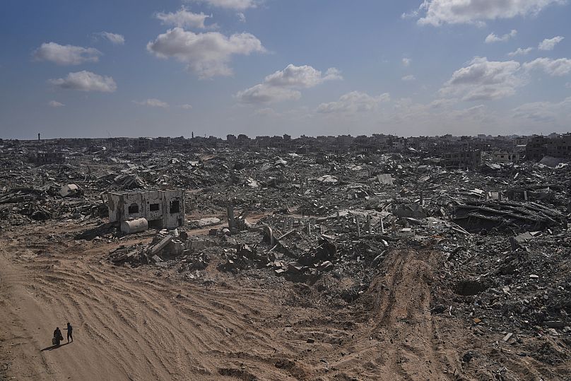 Deux Palestiniens déplacés passent devant des bâtiments détruits dans le quartier très endommagé de Sheikh Radwan, dans la ville de Gaza, le 11 octobre 2025.