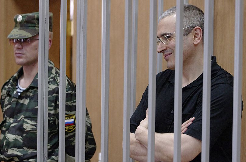 Бывший глава ЮКОСа Михаил Ходорковский улыбается из-за решетки во время судебного заседания в Москве, 3 августа 2004 года