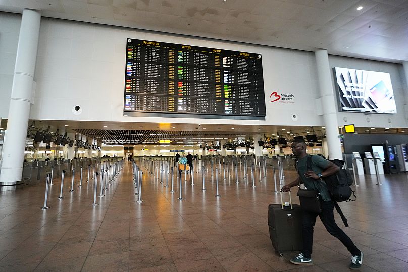 A man walks through an empty terminal with a departure board of cancelled flights at Brussels International Airport in Zaventem, 14 October, 2025 
