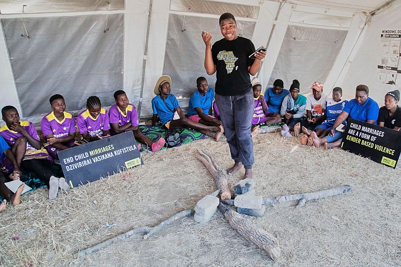 Women and girls sit inside a tent with a fireplace in the middle as their mentor speaks about child marriages at a school in Shamva, Zimbabwe, 29 August 2025